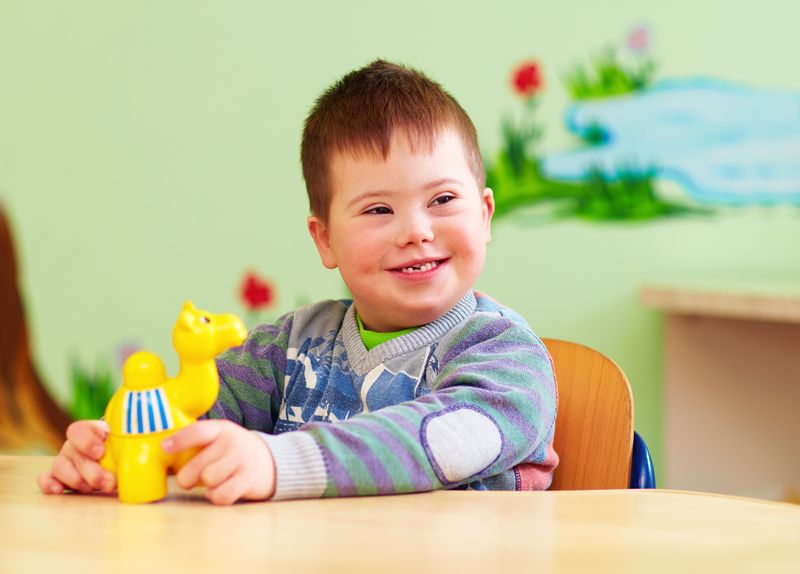 A smiling preschool boy plays with a toy at a classroom table.