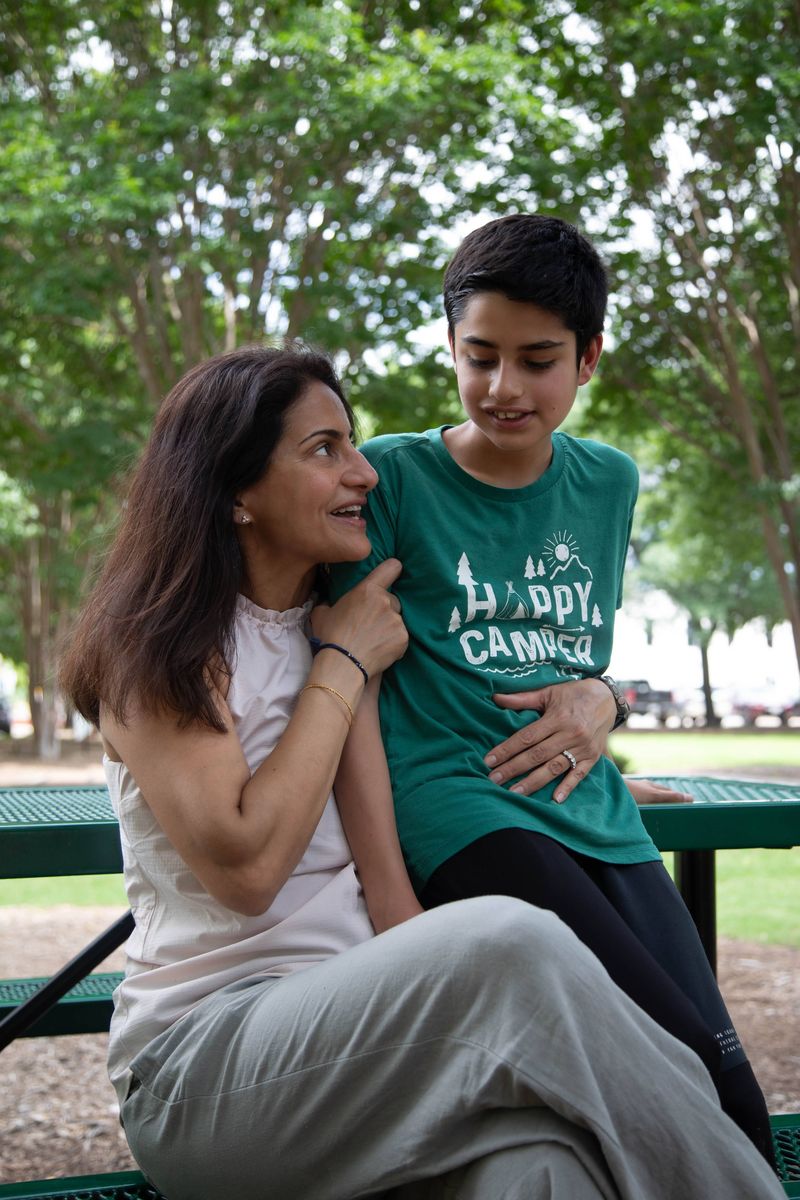 A mother laughs with her son on a park bench.