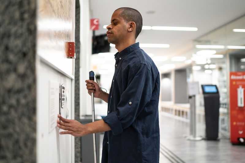 A man uses a white cane and reaches for elevator buttons.