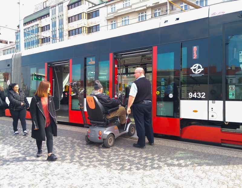 A wheelchair user rolls onto a city tram while others board.